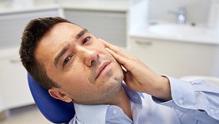 Man in dental chair holding cheek