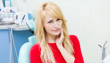 Woman in dental chair holding jaw