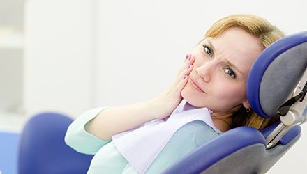 Woman in dental chair holding cheek